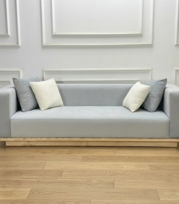 Ảnh chụp trực diện bộ Sofa Komorebi trong bối cảnh phòng khách tối giản. Ánh sáng tự nhiên chiếu từ một bên làm nổi bật vân gỗ Tần Bì ở chân đế và bề mặt nỉ mềm mại. Góc nhìn này khoe trọn vẹn tỉ lệ cân đối và vẻ đẹp thanh thoát của sản phẩm