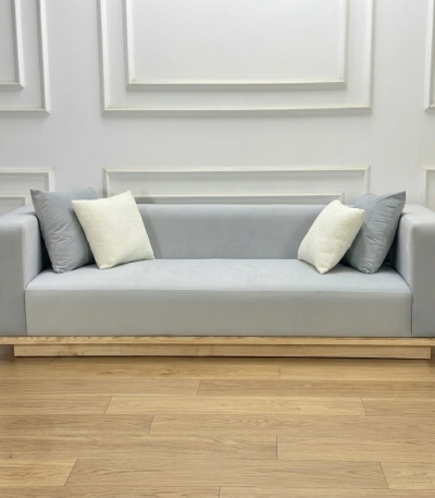 Ảnh chụp trực diện bộ Sofa Komorebi trong bối cảnh phòng khách tối giản. Ánh sáng tự nhiên chiếu từ một bên làm nổi bật vân gỗ Tần Bì ở chân đế và bề mặt nỉ mềm mại. Góc nhìn này khoe trọn vẹn tỉ lệ cân đối và vẻ đẹp thanh thoát của sản phẩm