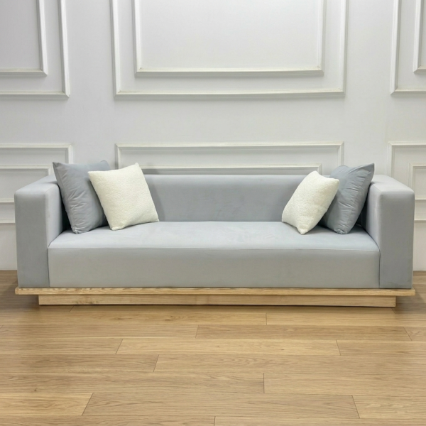 Ảnh chụp trực diện bộ Sofa Komorebi trong bối cảnh phòng khách tối giản. Ánh sáng tự nhiên chiếu từ một bên làm nổi bật vân gỗ Tần Bì ở chân đế và bề mặt nỉ mềm mại. Góc nhìn này khoe trọn vẹn tỉ lệ cân đối và vẻ đẹp thanh thoát của sản phẩm